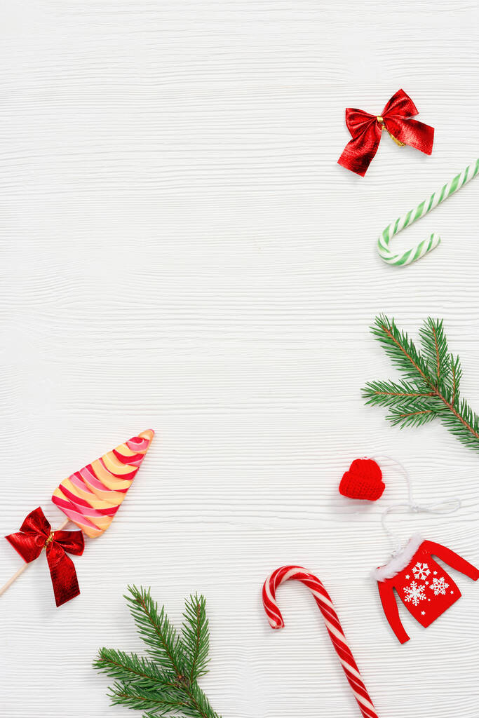 Composición navideña. Dulces de Navidad y bastones de caramelo, ramas de pino y juguetes de madera de Año Nuevo en la mesa blanca, vista superior, posición plana. - Foto, imagen