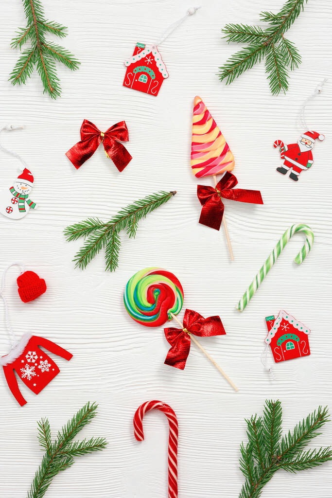 Різдвяні цукерки різноманітний вид зверху, зелені ялинкові гілки, дерев'яні іграшки на білому тлі, плоска лежа. Яскраві новорічні цукерки та льодяники
. - Фото, зображення