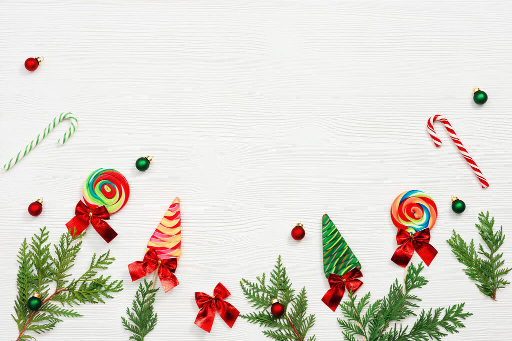 Рождественская композиция Рождественские сладости и леденцы, ветки туи, и новогодние маленькие красные и зеленые шарики на белом деревянном столе, вид сверху, плоский лежал. - Фото, изображение