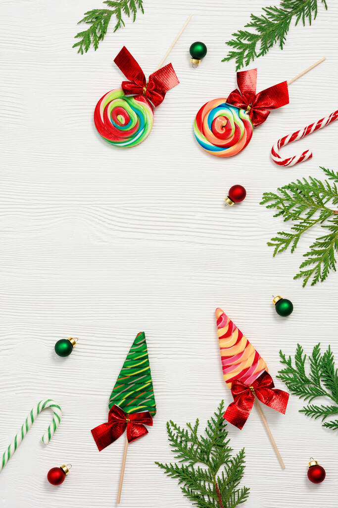 Різдвяна композиція. Різдвяні цукерки та цукерки, гілки туї та новорічні маленькі червоні та зелені кульки на білому дерев'яному столі, вид зверху, плоска покладена
. - Фото, зображення