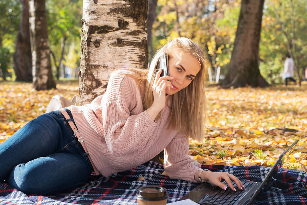 Fiatal nő dolgozik laptop a szabadban, és beszél telefonon. - Fotó, kép