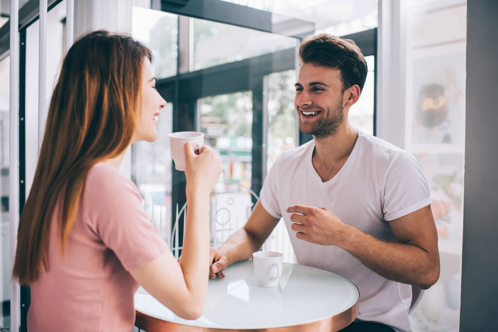 Τρυφερό ρομαντικό ζευγάρι πίνοντας καφέ μαζί και μιλώντας ευτυχισμένα, ενώ περνούν υπέροχο χρόνο στο καφέ κοιτάζοντας ο ένας τον άλλο - Φωτογραφία, εικόνα