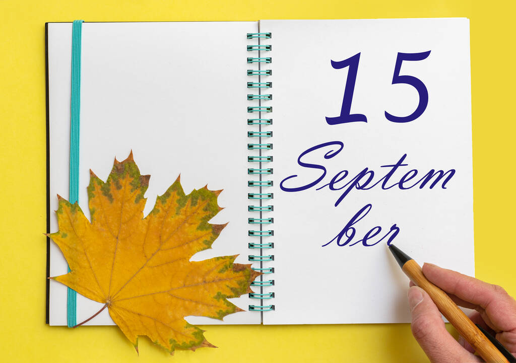 15 de septiembre. 15 de septiembre. Mano escribiendo la fecha 15 de septiembre en un cuaderno abierto con una hermosa hoja de arce natural sobre un fondo amarillo. Mes de otoño, concepto del día del año. - Foto, Imagen