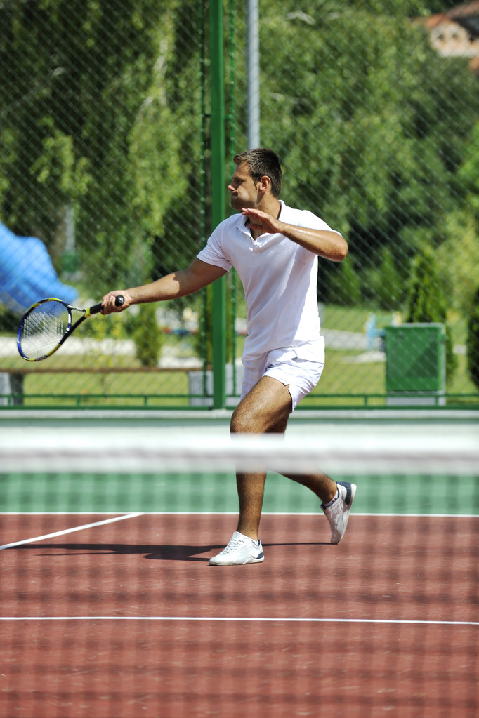 Jovem joga tênis ao ar livre no campo de ténis laranja no início da manhã
 - Foto, Imagem