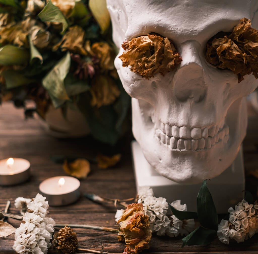 Egy csokor hervadt virág gyertyákkal az asztalon és egy koponya.. - Fotó, kép