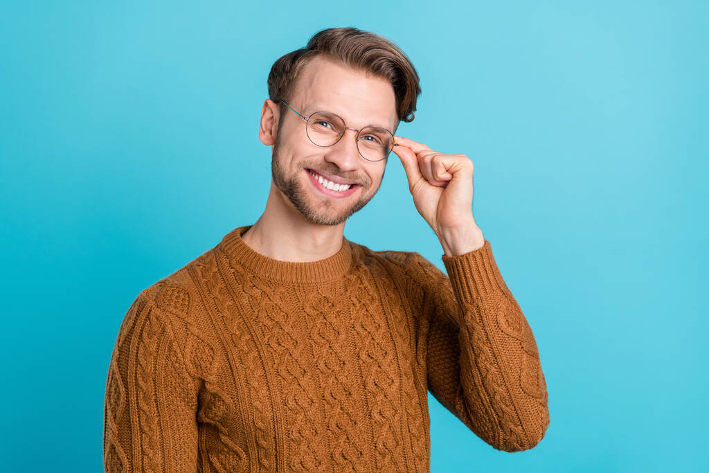 Foto de divertido encantador caballero joven usar gafas de brazo de jersey marrón sonriendo aislado fondo de color azul - Foto, Imagen