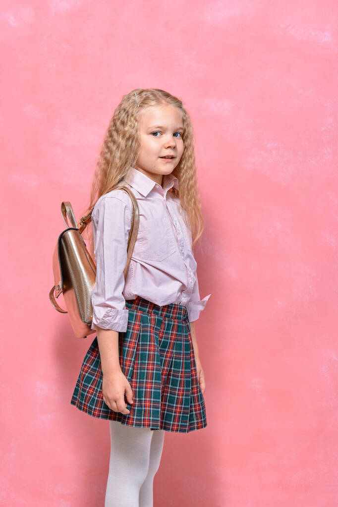 πορτραίτο του μικρού κοριτσιού με σακίδιο. Μαθήτρια με στολή. ροζ φόντο - Φωτογραφία, εικόνα