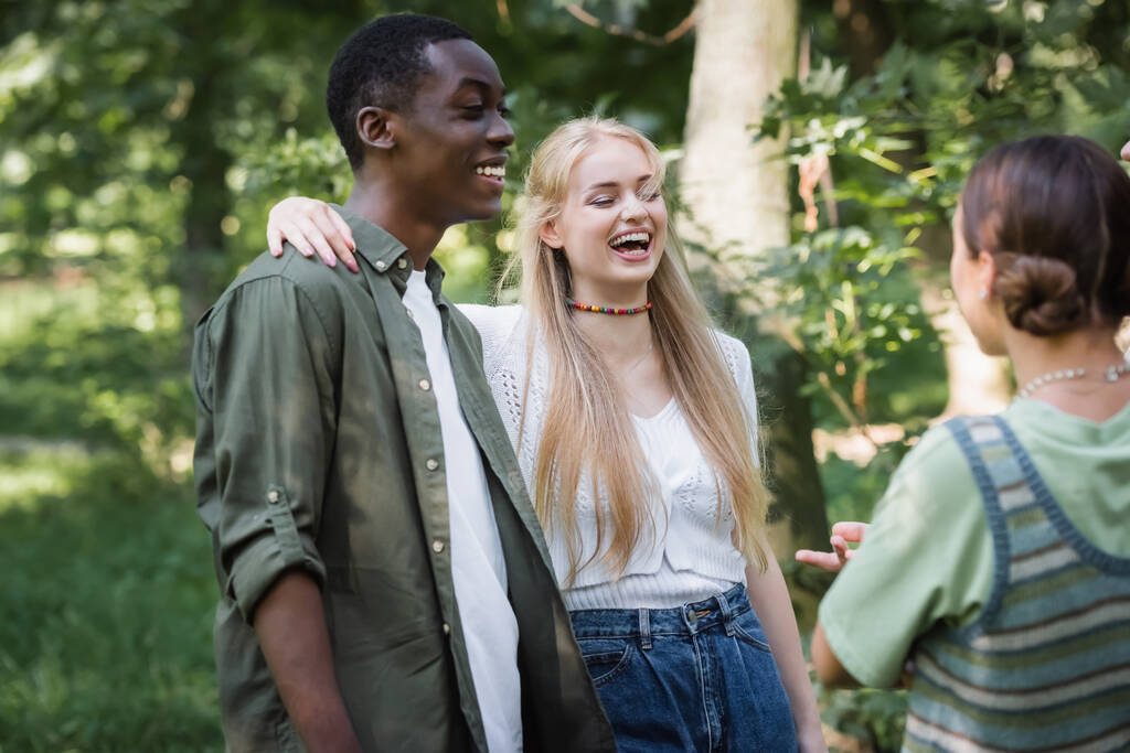 glimlachen tiener meisje knuffelen afrikaanse amerikaanse vriend in park  - Foto, afbeelding