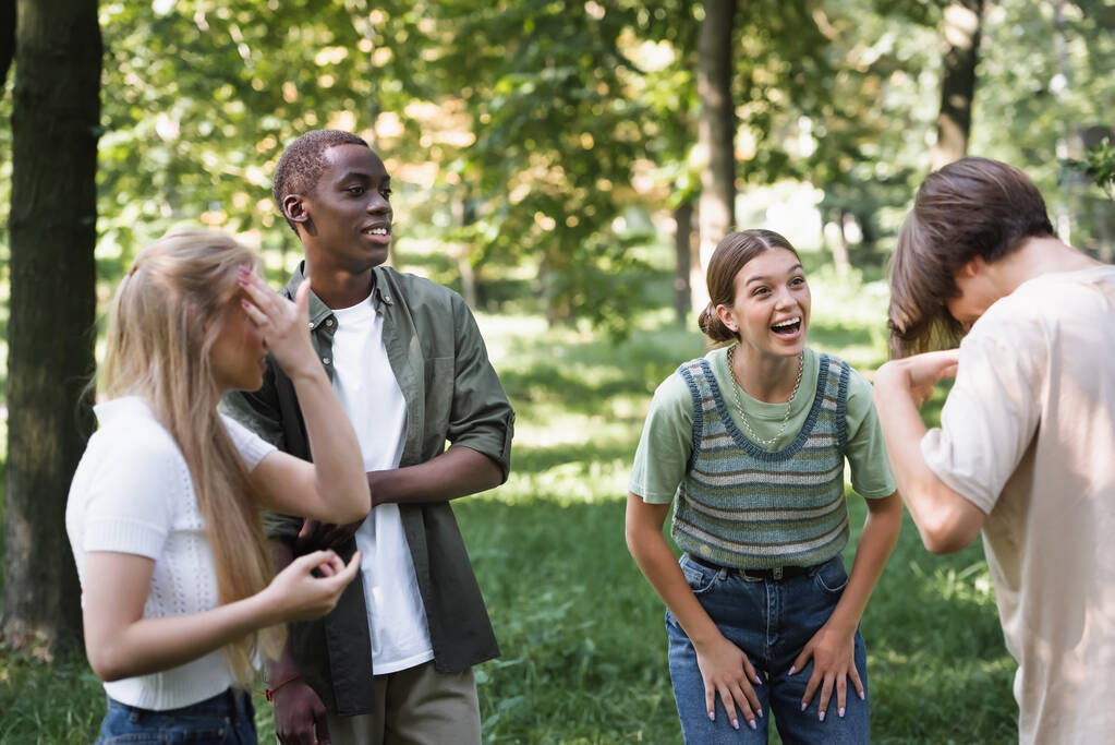 Sonriente chica mirando amigo cerca multiétnico adolescentes en parque  - Foto, imagen
