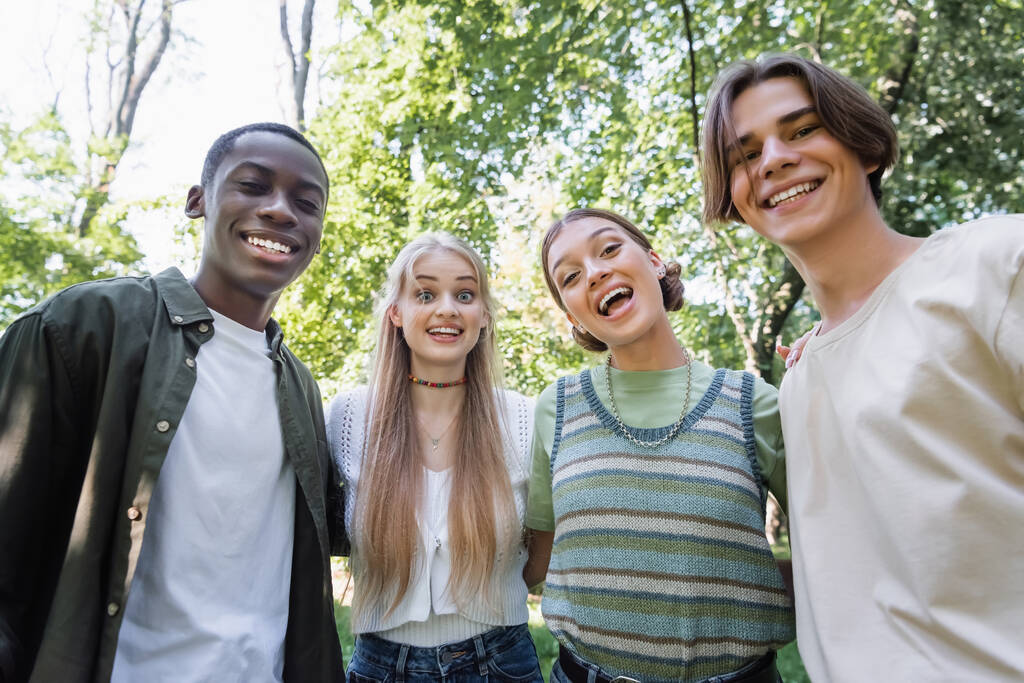 Adolescentes multiétnicos alegres olhando para a câmera ao ar livre  - Foto, Imagem