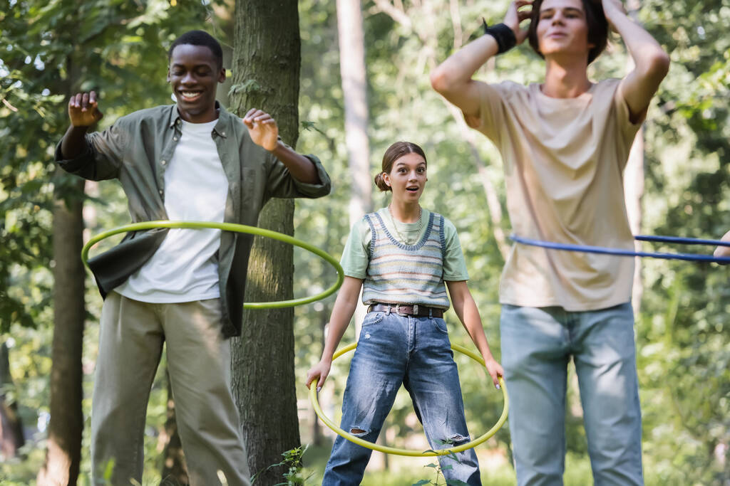 Excited girl holding hula hoop near blurred interracial friends  - Photo, Image