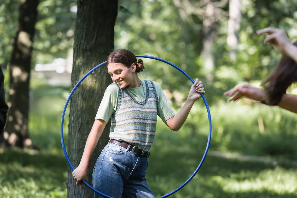 Smiling teenager holding hula hoop in park  - Photo, Image
