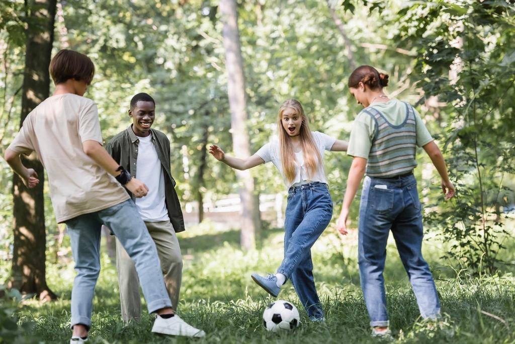 Garota excitada jogando futebol com adolescentes multiétnicos no parque  - Foto, Imagem