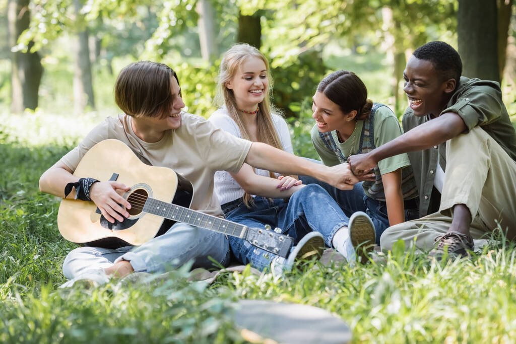 Mezirasoví teenageři s akustickou kytaru dělat pěsti nárazu v parku  - Fotografie, Obrázek