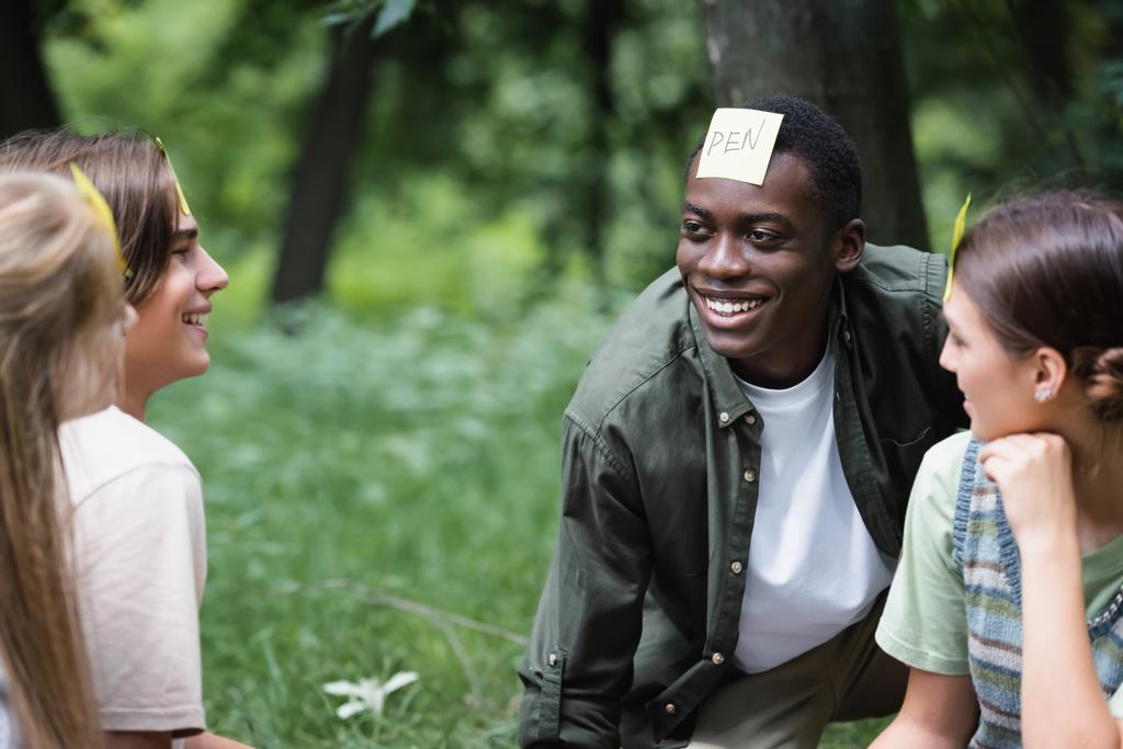 Adolescents interracial joyeux avec des autocollants jouer qui je suis dans le parc  - Photo, image