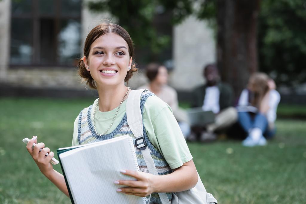 Χαμογελώντας φοιτητής με smartphone και notebook σε εξωτερικούς χώρους  - Φωτογραφία, εικόνα