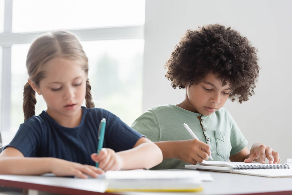 interrazziale bambini scrittura in notebook durante la lezione - Foto, immagini