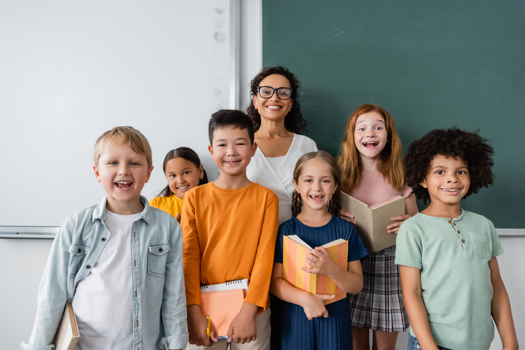 Afrikaans amerikaans leraar en vreugdevolle multi-etnische schoolkinderen glimlachen op camera in de klas - Foto, afbeelding