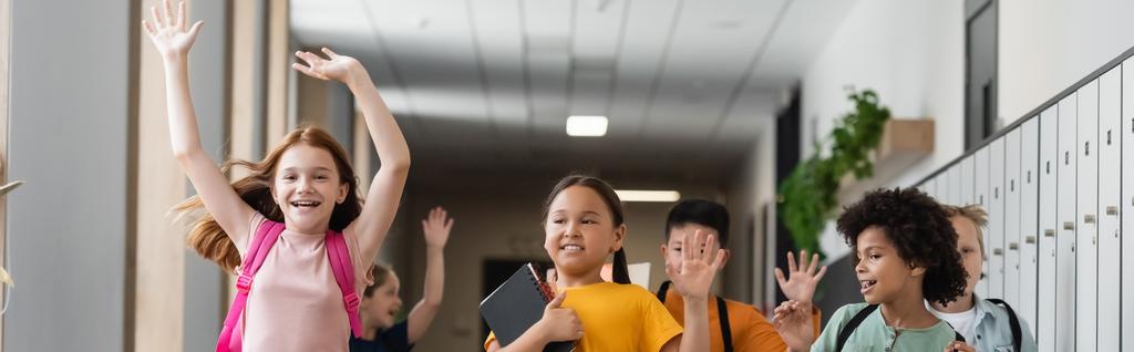 niños alegres multiculturales agitando las manos en el pasillo escolar, pancarta - Foto, imagen