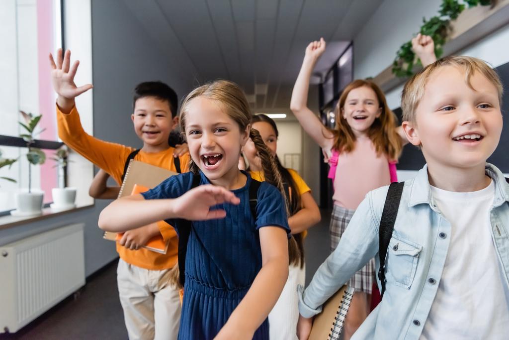 схвильовані багатоетнічні однокласники махають руками і показують жест виграшу в шкільному залі
 - Фото, зображення