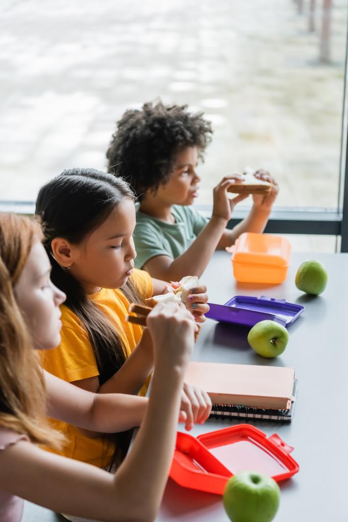 багатоетнічні діти їдять бутерброди на обід у школі
 - Фото, зображення