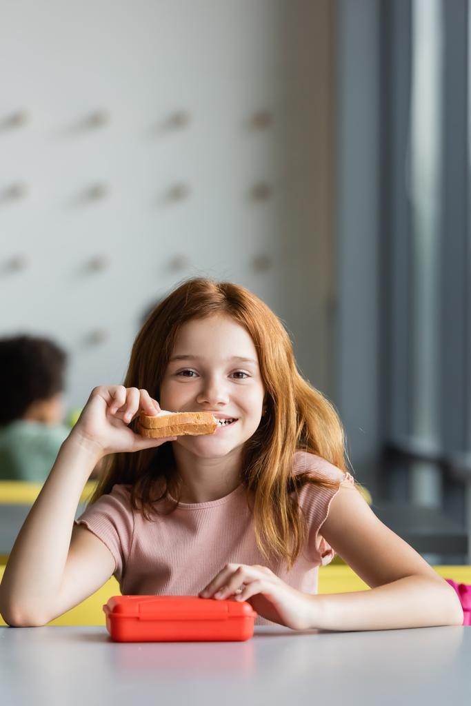 szczęśliwy uczennica jedzenie kanapki podczas przerwy obiadowej w szkole - Zdjęcie, obraz