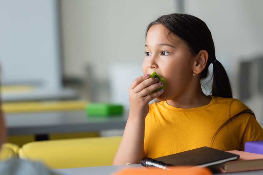 asiático escolar comer manzana durante almuerzo descanso en escuela eatery - Foto, imagen