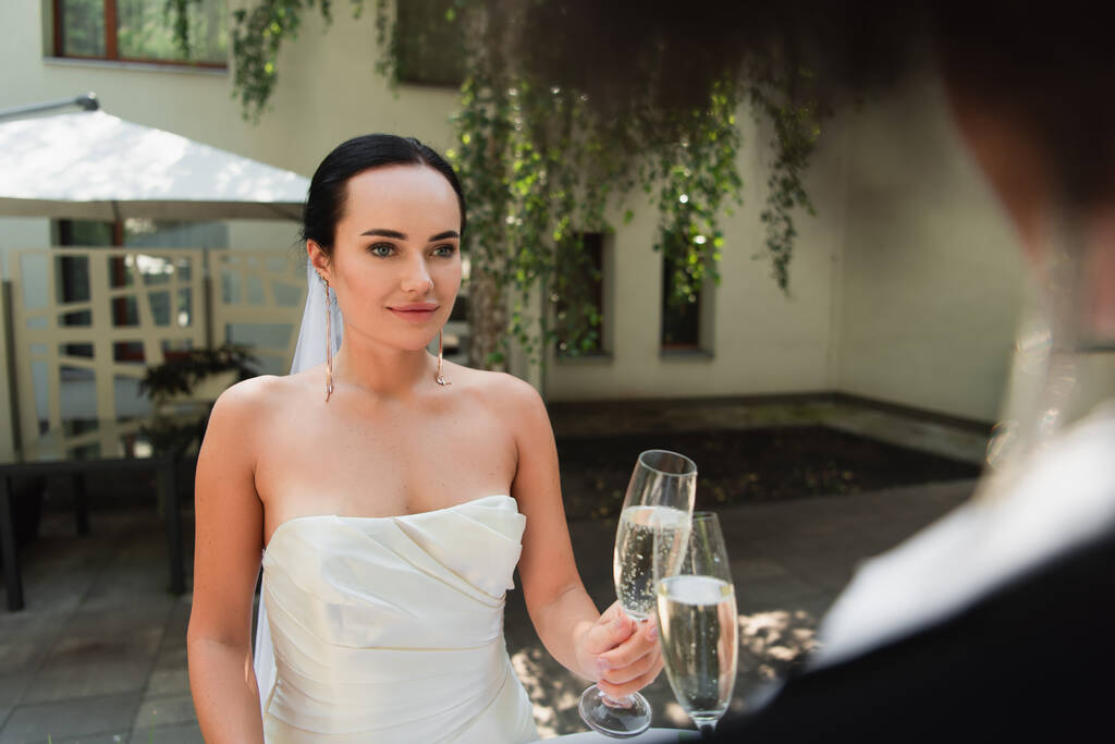 Donna in abito da sposa brindare champagne con fidanzata offuscata durante il matrimonio all'aperto  - Foto, immagini