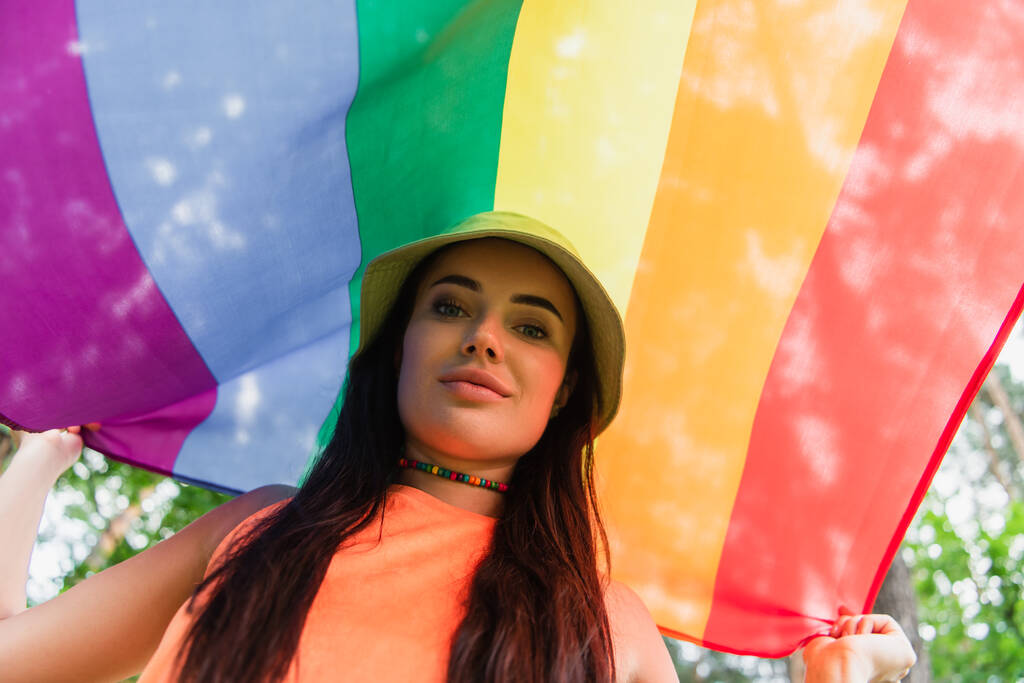 Low angle view of young woman holding lgbt flag outdoors  - Photo, Image