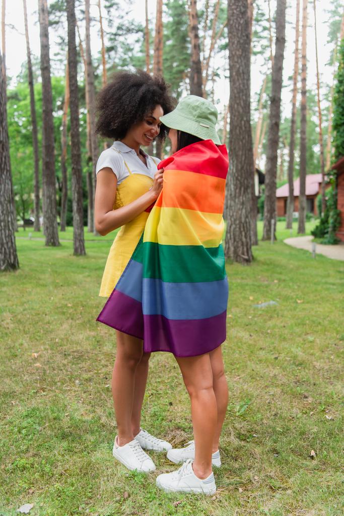 Позитивная африканская американка обнимает подружку в парке под флагом "lgbt"  - Фото, изображение