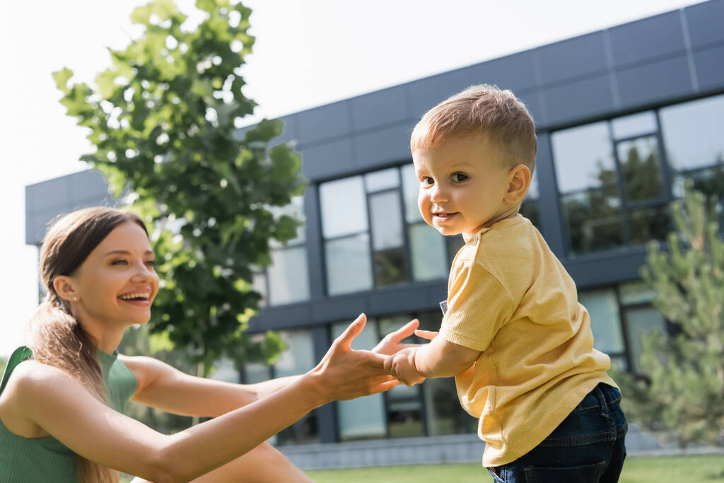 cheerful mother holding hands with toddler son outside  - Photo, Image
