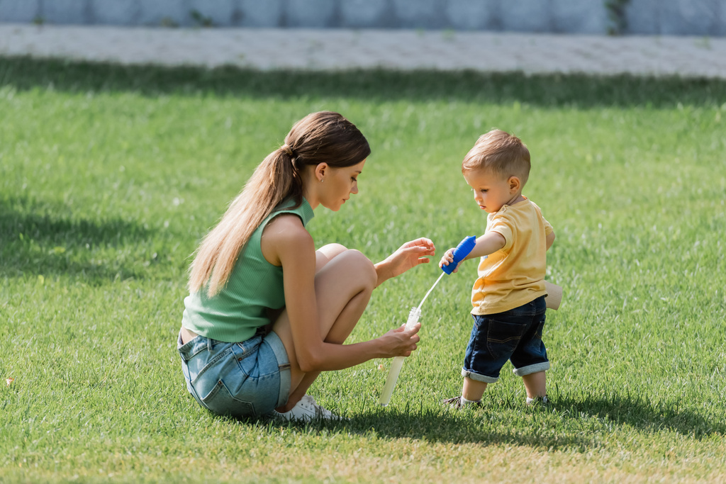 Nuori äiti tilalla saippuakupla pullo lähellä lapsi poika ruoho - Valokuva, kuva