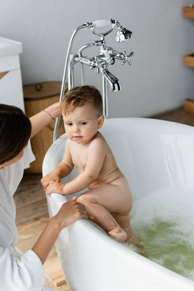 мать смотрит на малыша сына в ванной  - Фото, изображение
