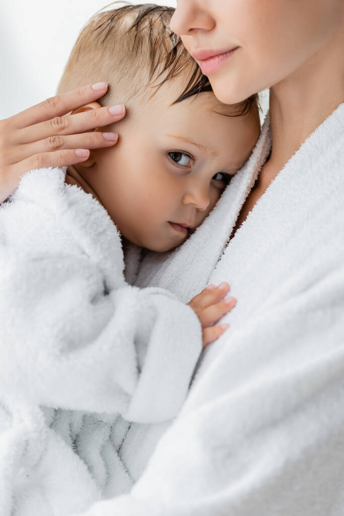 close up de jovem mãe segurando em braços criança filho em roupão de banho - Foto, Imagem