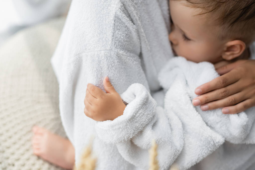 madre abrazando hijo pequeño con los ojos cerrados en albornoz - Foto, Imagen