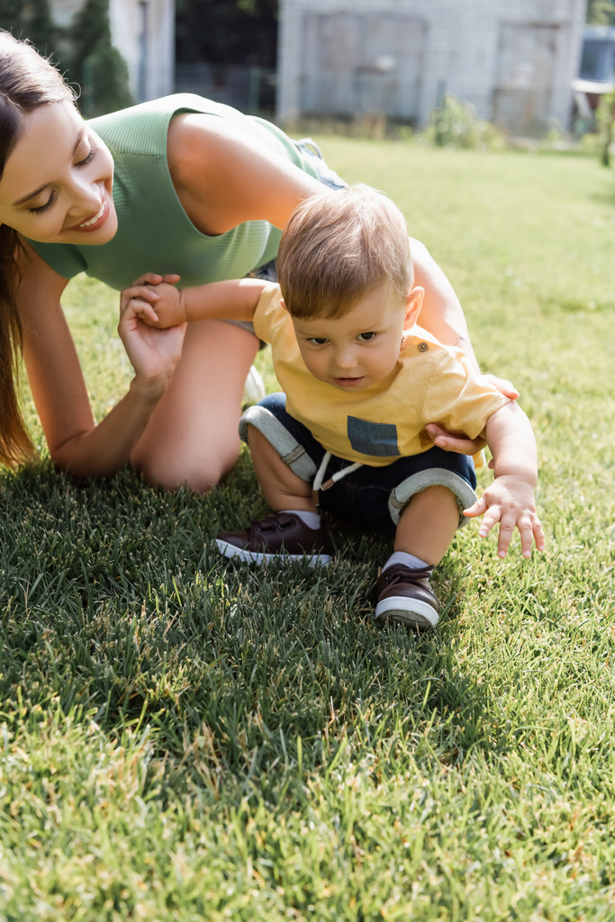 щаслива мати дивиться на маленького сина, що сидить на зеленій траві
  - Фото, зображення