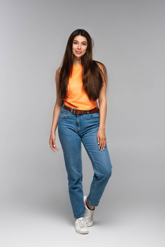 полная длина веселой молодой женщины в джинсах в джинсах в джинсах, позирующей на сером - Фото, изображение