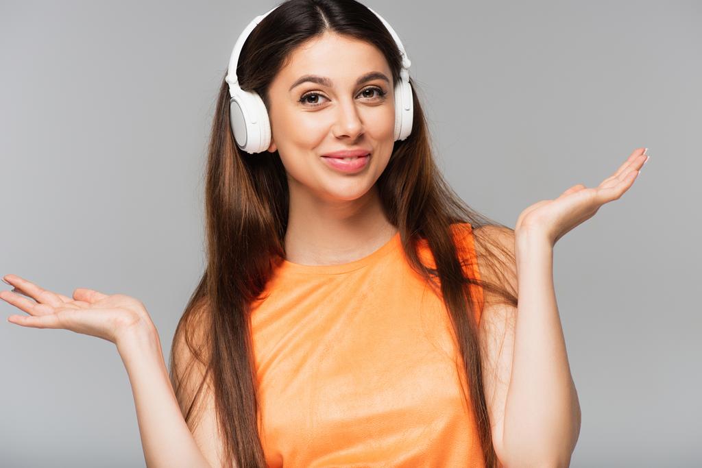 χαρούμενη νεαρή γυναίκα με ασύρματα ακουστικά που ακούει μουσική απομονωμένη σε γκρι - Φωτογραφία, εικόνα