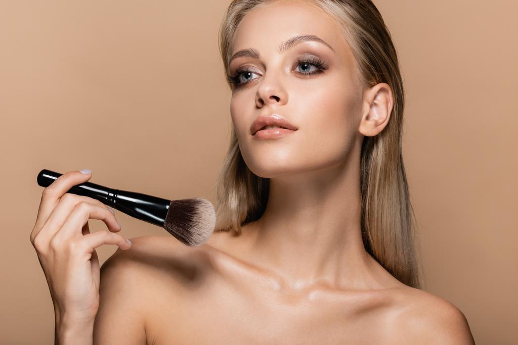 blondýny žena s make-upem na dokonalé tváři drží měkký kosmetický kartáč izolované na béžové - Fotografie, Obrázek