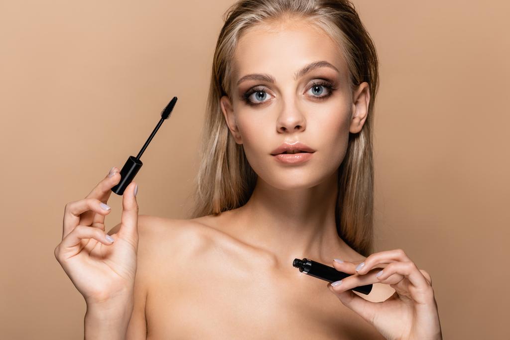 pretty woman with blonde hair and naked shoulders holding black mascara isolated on beige - Photo, Image
