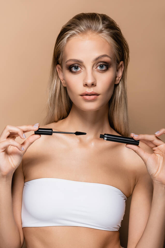 young woman with makeup showing black mascara isolated on beige - Photo, Image