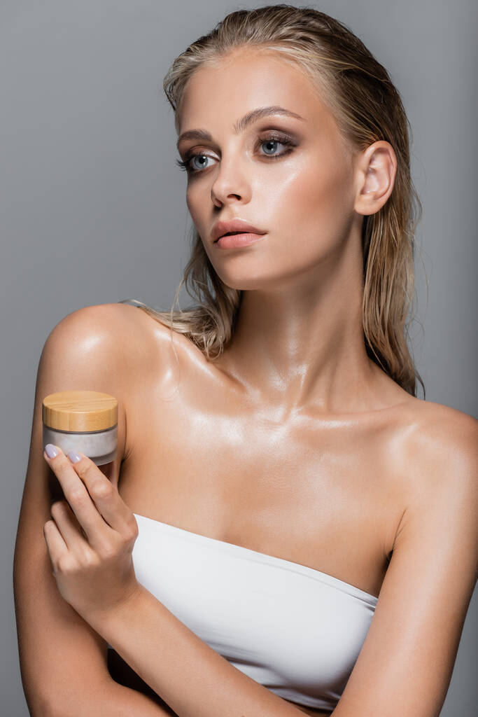 wet woman with blonde hair holding cosmetic cream isolated on grey - Photo, Image