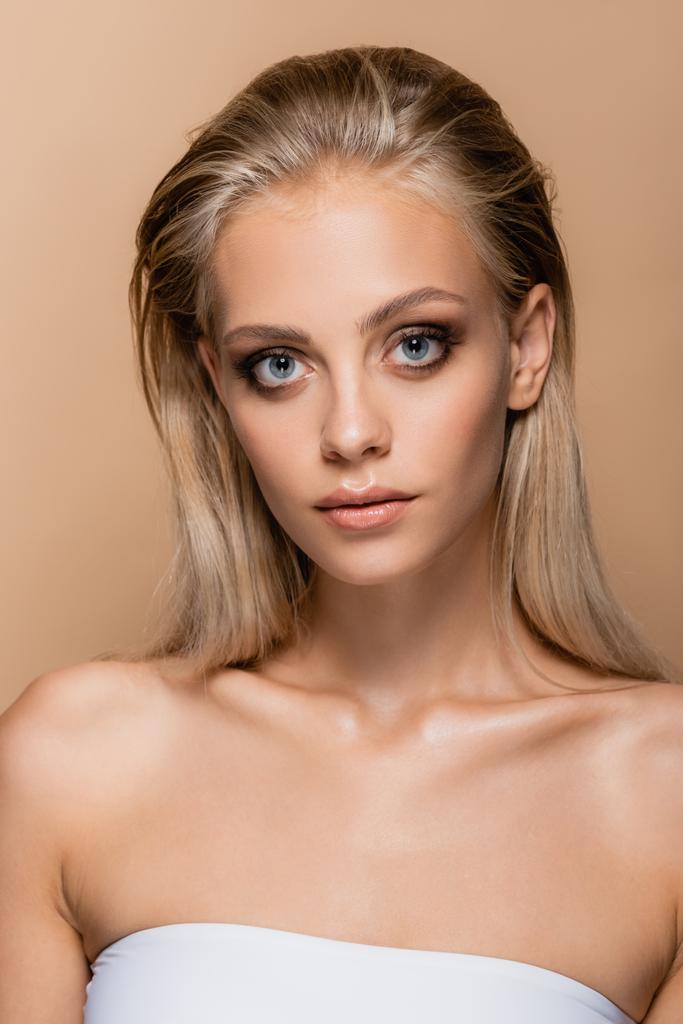 junge Frau mit perfektem Gesicht und perfektem Make-up blickt vereinzelt in die Kamera auf beige - Foto, Bild