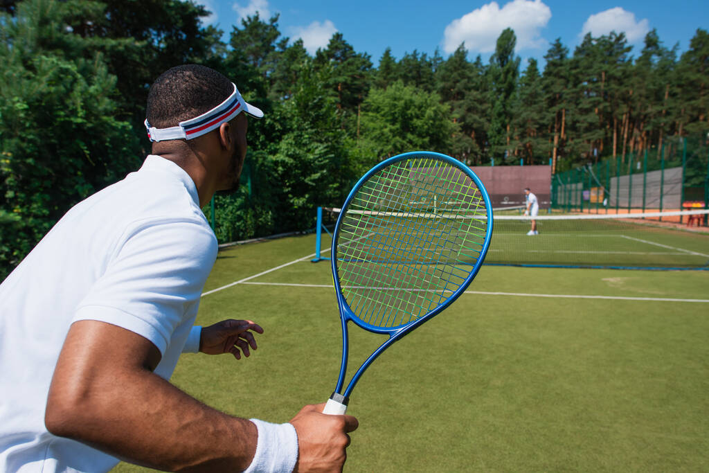 Deportista afroamericano jugando al tenis con un amigo borroso en la cancha  - Foto, Imagen