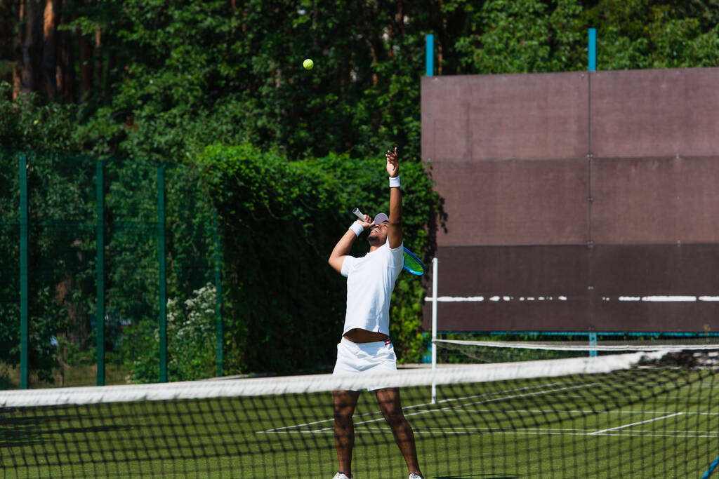 Africano americano desportista segurando raquete perto de bola no campo  - Foto, Imagem