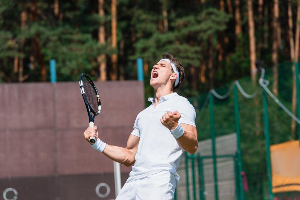 Aufgeregter Sportler mit Tennisschläger zeigt Ja-Geste auf dem Platz  - Foto, Bild
