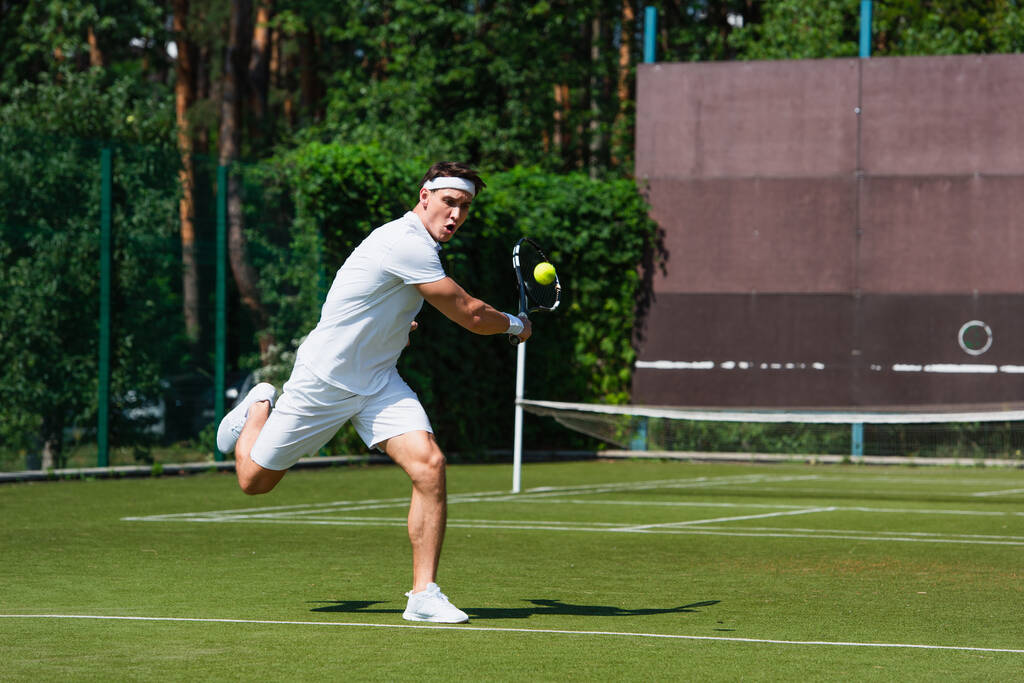 Jonge sportman loopt tijdens het spelen van tennis op het veld  - Foto, afbeelding
