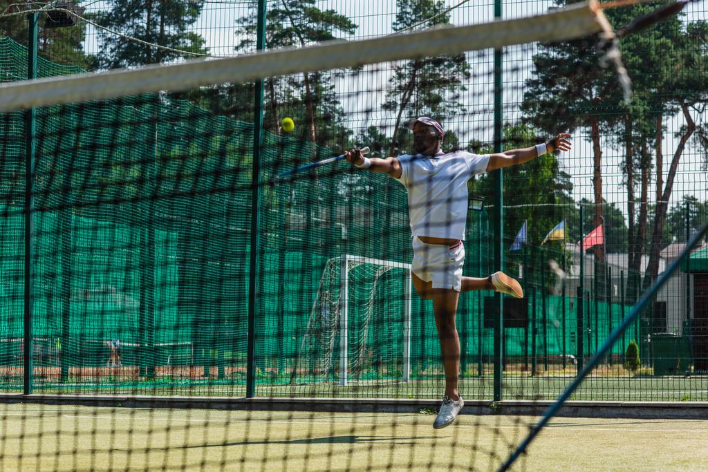 Afrykański amerykański sportowiec skacze podczas gry w tenisa w pobliżu sieci  - Zdjęcie, obraz