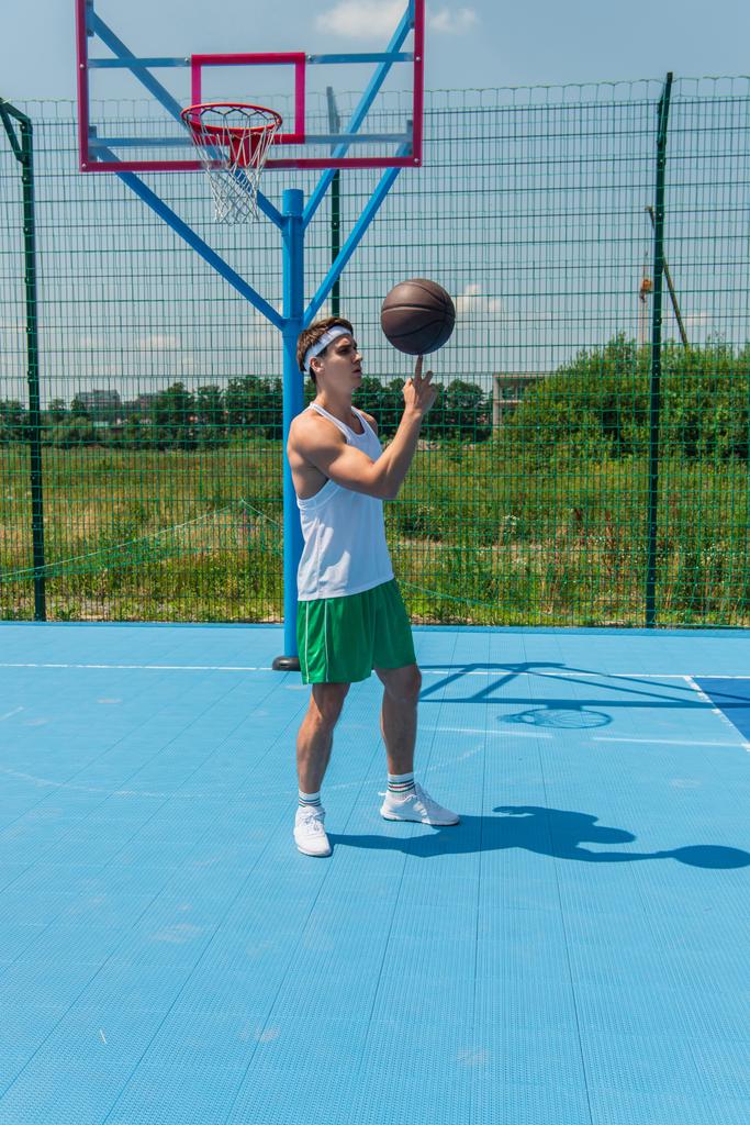 Jeune sportif filant ballon de basket sur le doigt sur le terrain de jeu  - Photo, image