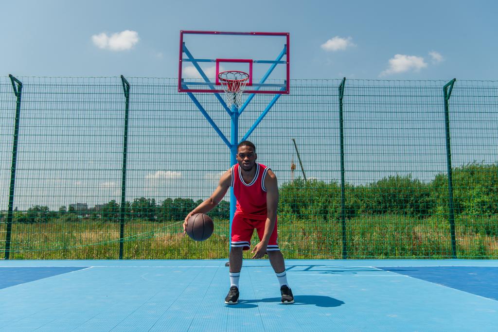 African american man looking at camera while playing streetball on playground  - Photo, Image